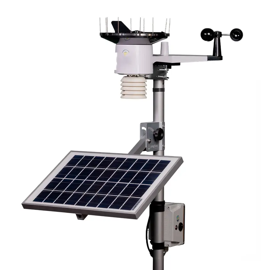 Estação meteorológica profissional: cabeça de sensores no topo, anemômetro e biruta num braço lateral, painel solar angulado e caixa registradora no mastro.